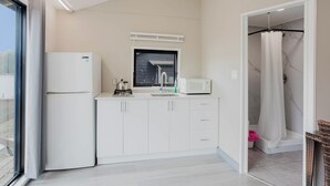 Une cuisine moderne avec des meubles blancs, un réfrigérateur, un four à micro-ondes et une fenêtre équipée de stores.