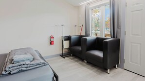 A room with a bed, a sofa, a window with curtains, a fire extinguisher, and a heater. - 1 Bedroom Cottage IX: PL (Gravenhurst)