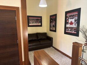 Ein Zimmer mit einer dunkelbraunen Tür, einem schwarzen Ledersofa, einem weißen, flauschigen Teppich und drei gerahmten Bildern an der Wand.