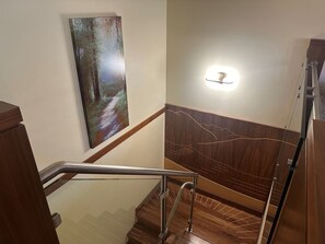 A wooden staircase with a handrail, a wall-mounted light fixture, and a painting of a forest scene. -  Greyhawk on Blueberry Hill —  2 bdrm 2 bath with private balcony (Whistler)
