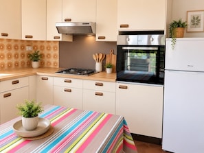 A modern kitchen with white cabinetry, a stainless steel range hood, a built-in oven, and a refrigerator. - Domaine de la Barthe - Spacious Apartment in a Vineyard (Béziers)