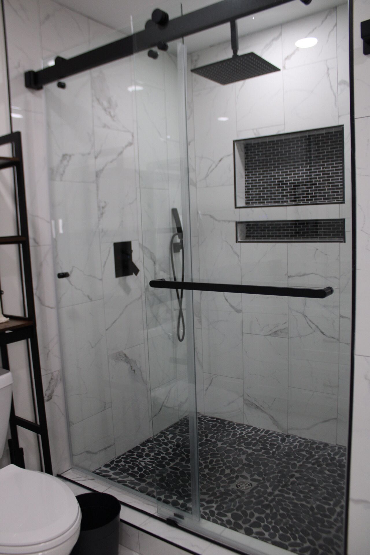 A glass-enclosed shower with a marble floor, a towel rack, and a small window.