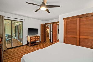 Ein Schlafzimmer mit einem Bett, einem Holzschrank, einem Fernseher auf einem Holztisch und einem Deckenventilator.