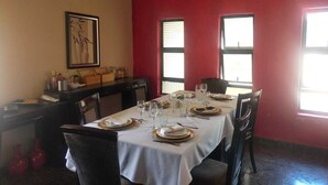 A dining area with a table set for four, chairs, a painting on the wall, and two windows.