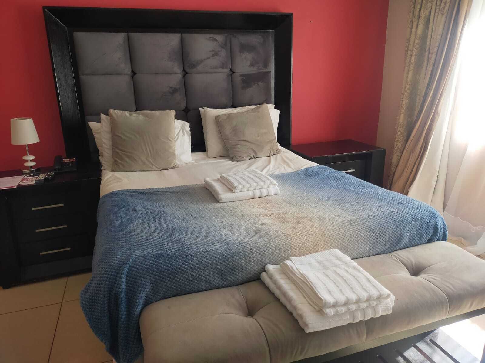 A bedroom with a tufted headboard, a bed with beige bedding, a blue blanket, and two bedside tables with lamps.