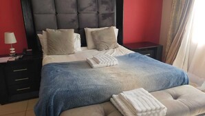 A bedroom with a tufted headboard, a bed with beige bedding, a blue blanket, and two bedside tables with lamps.