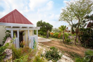 Una casa con techo rojo, un porche blanco y un jardín con diversas plantas y árboles.