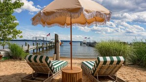 Un cadre idyllique en bord de mer, avec deux fauteuils de jardin en osier, une table ronde en bois et un parasol beige.