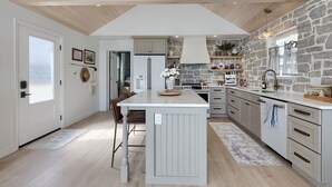 Une cuisine moderne dotée d’un îlot central, d’un mur recouvert de pierres apparentes et d’un plafond en bois.