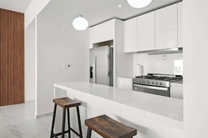 Eine moderne Küche mit weißen Schränken, einem Edelstahl-Kühlschrank, einem Gasherd und zwei Holzbarhocker.