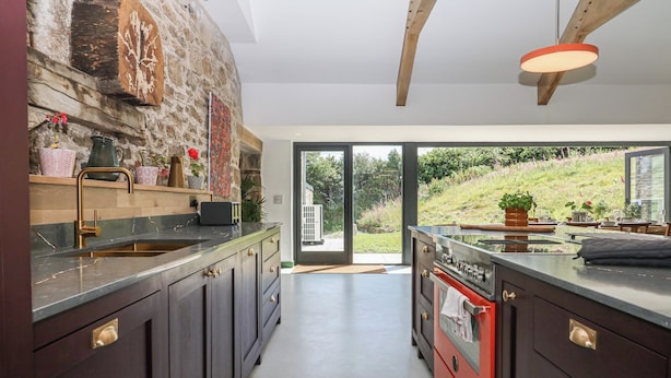 Une cuisine moderne avec des meubles de couleur sombre, un mur d’accent en pierre et une grande fenêtre donnant sur un jardin.