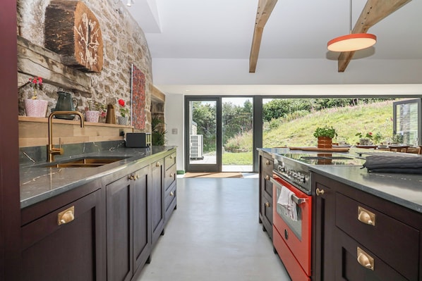 A modern kitchen with dark cabinetry, a stone accent wall, and a large window overlooking a garden.