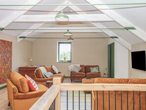 Un loft con techo inclinado, vigas de madera, un ventanal grande y un televisor montado en la pared.
