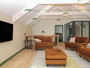 A spacious living room with a high ceiling, wooden flooring, and a large flat-screen TV mounted on the wall.
