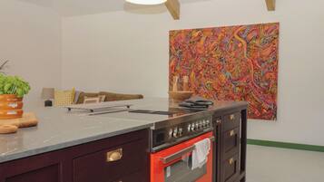 Une cuisine moderne dotée d’un grand îlot central, d’un four rouge et d’une peinture abstraite aux couleurs vives accrochée au mur.