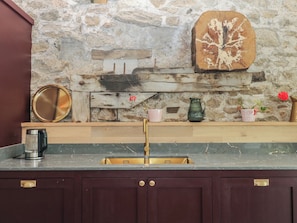 A kitchen with a stone wall, wooden shelf, and a sink. - Reddaway Threshing Barn (Okehampton)