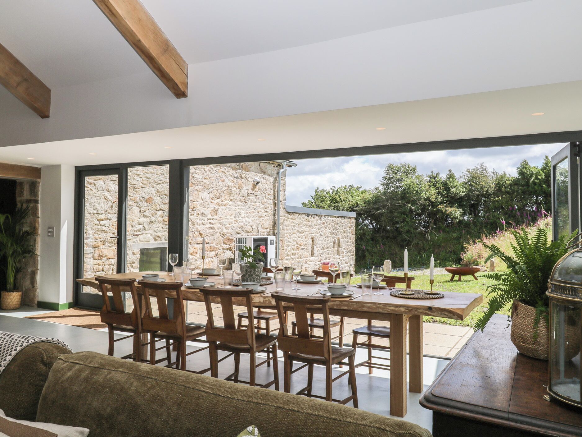 Un comedor moderno con un fondo de pared de piedra, una mesa de madera preparada para comer y vistas al jardín.