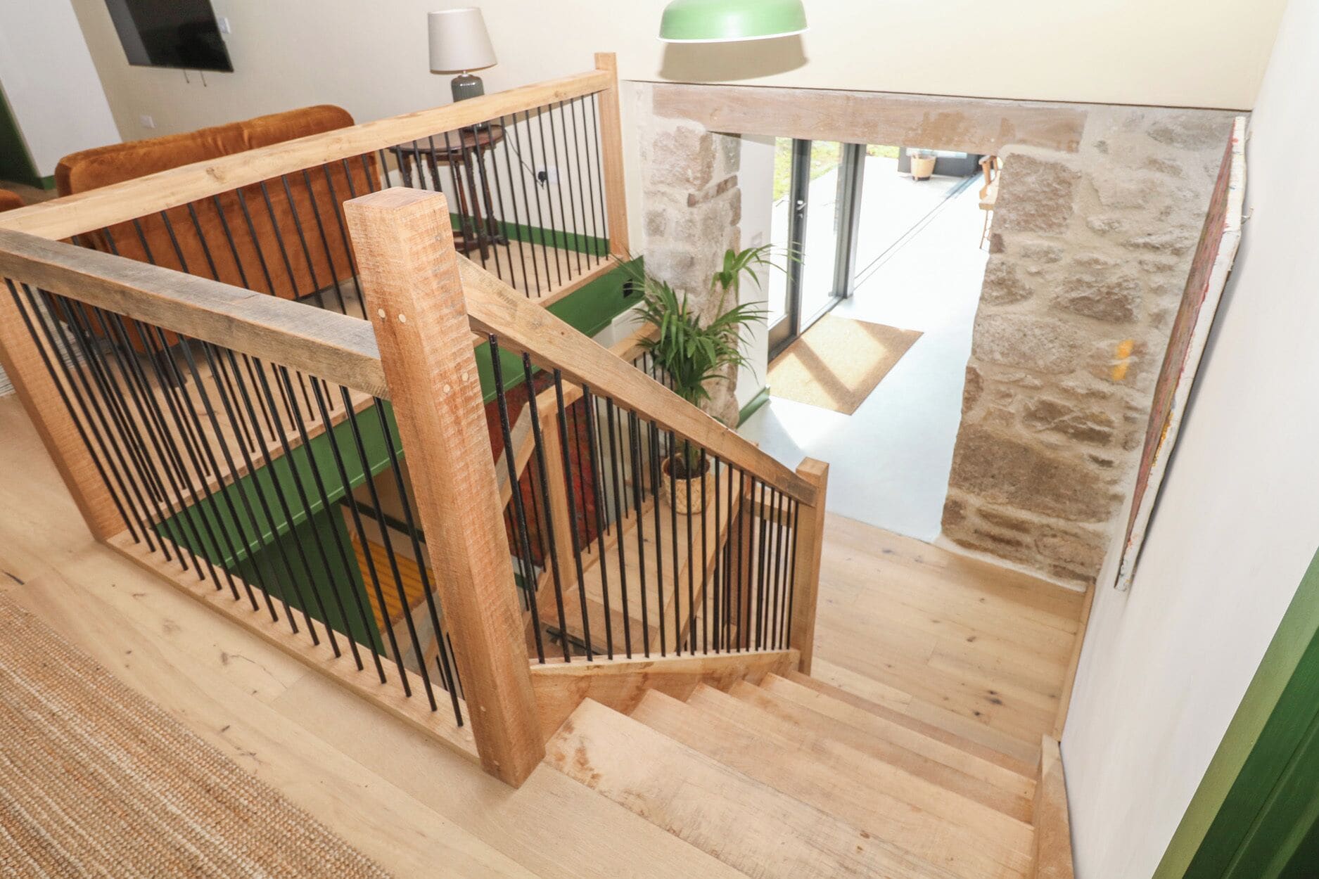A wooden staircase with a metal railing, a stone wall, and a hanging light fixture.