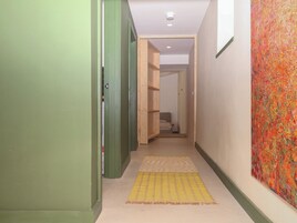 Un pasillo estrecho con paredes verdes, un tapete a rayas amarillas y un cuadro abstracto de colores en la pared derecha.