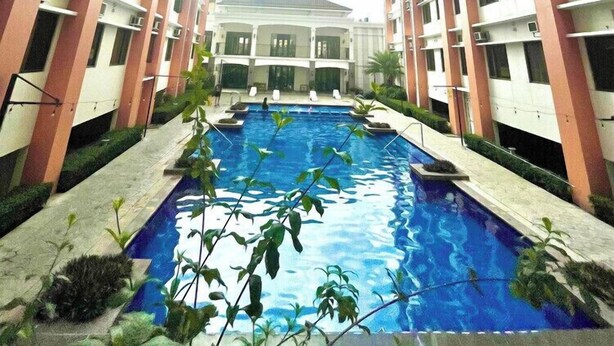 A multi-story hotel with a central swimming pool, surrounded by greenery and a clear sky. - Serene Stay at Paseo Verde (Las Piñas)
