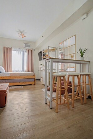 Ein Schlafzimmer mit einem Bett, einem Schreibtisch mit Hocker, einem Deckenventilator und einem Fenster mit Vorhängen.