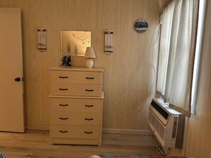 Une pièce avec un mur en bois, une commode blanche avec des tiroirs, un miroir, une horloge et un appareil de climatisation.
