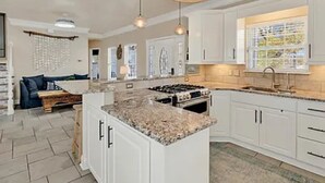 A spacious kitchen with white cabinets, a granite countertop, and a large island. There is a dining area with a sofa and a coffee table. - Ocean Views, 5 min walk to Beach, Waterpark, Arcade, Store ~ 5 bd/3; Sleeps 10 (Myrtle Beach)
