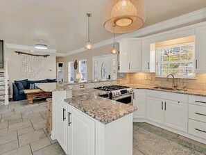 A spacious kitchen with white cabinets, a granite countertop, and a large island. There is a dining area with a sofa and a coffee table. - Ocean Views, 5 min walk to Beach, Waterpark, Arcade, Store ~ 5 bd/3; Sleeps 10 (Myrtle Beach)