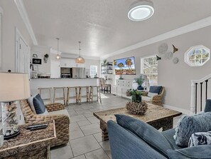 A modern living room with a sofa, coffee table, and a TV. There is a kitchen area with a bar and dining space. - Ocean Views, 5 min walk to Beach, Waterpark, Arcade, Store ~ 5 bd/3; Sleeps 10 (Myrtle Beach)