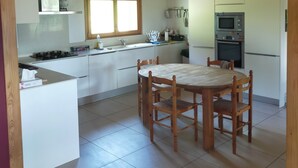 Une cuisine spacieuse avec un coin repas, des poutres en bois et une grande fenêtre.
