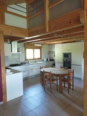 Una cocina amplia con comedor, vigas de madera y un ventanal grande.