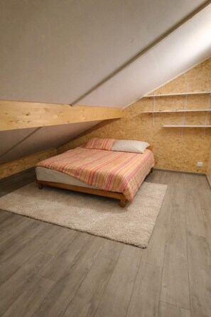 Un dormitorio con cama, piso de madera, alfombra blanca y vigas de madera a la vista.