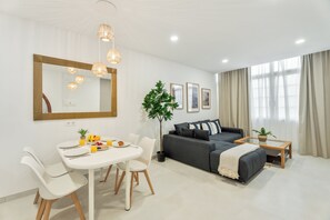 Ein modernes Wohnzimmer mit Essbereich, einem grauen Sofa, einem Couchtisch und einem großen Spiegel.