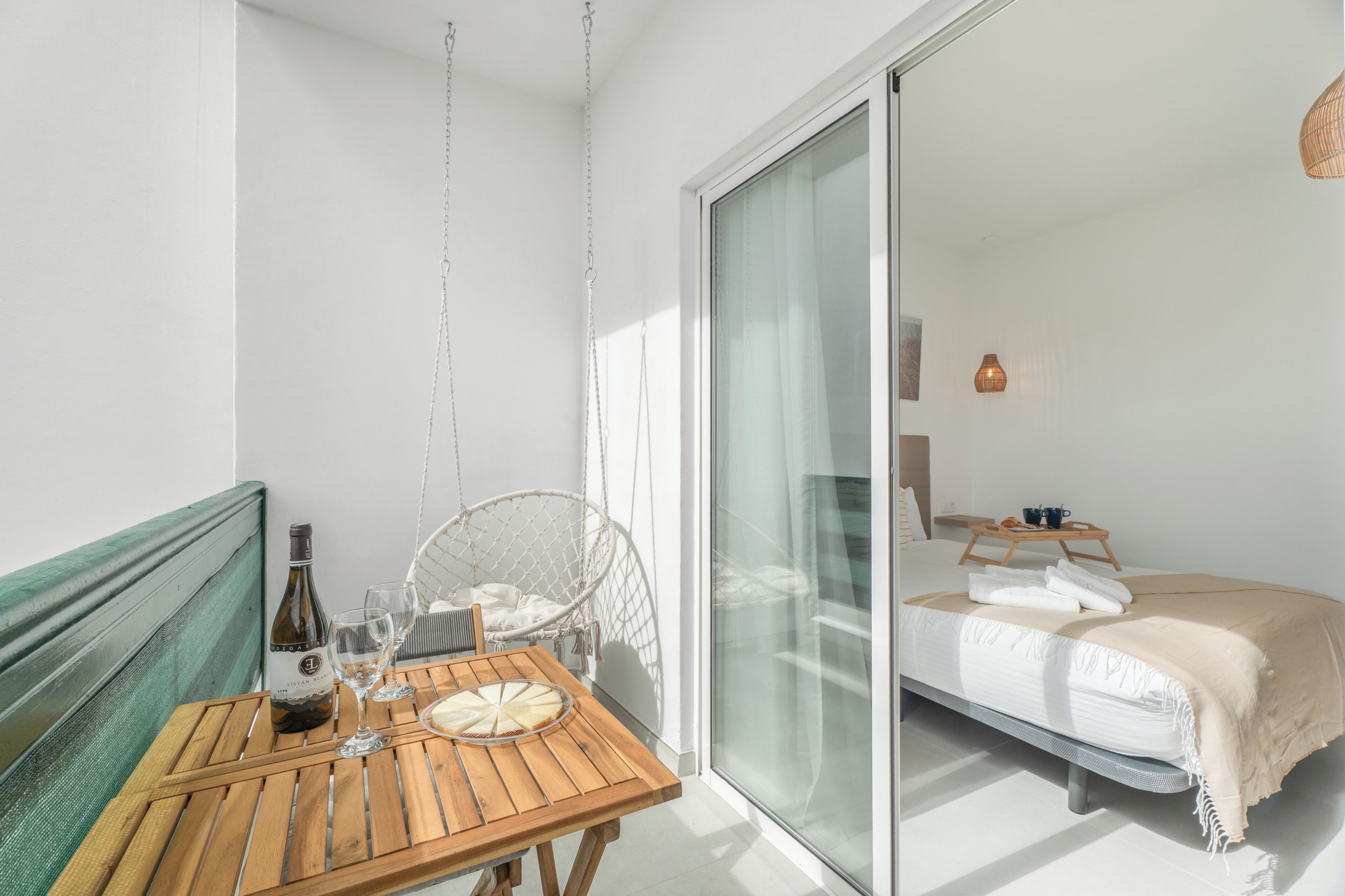 A balcony with a wooden table, a hanging chair, a bottle of wine, and a glass.