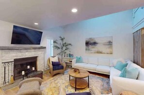A living room with a fireplace, a sofa, a coffee table, and a television mounted on the wall. - Lakeview 3 BR Townhome with Fireplace and Deck (Lake Harmony)