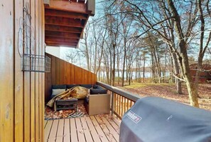 Une terrasse en bois avec un canapé, un barbecue et une vue sur les arbres et l’eau.