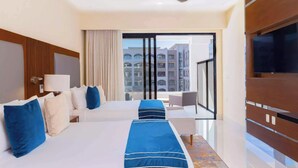 Ein Hotelzimmer mit zwei Betten, einem Fernseher, einem Deckenventilator und Blick auf Gebäude durch das Fenster.