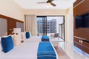 Une chambre d’hôtel avec deux lits, une télévision, un ventilateur de plafond et une vue sur les immeubles par la fenêtre.