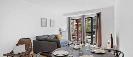A modern living room with a round dining table set for four, a sofa, a wicker chair, and a television.