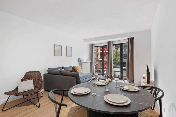 Welcoming living and dining space with a round table, cosy seating and armchairs — a sociable spot to relax in this stylish Knokke holiday apartment.