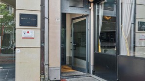 Entrada de um edifício com porta de vidro, uma placa indicando 'Monte Catini 139' e uma pequena placa com o símbolo de uma bicicleta.