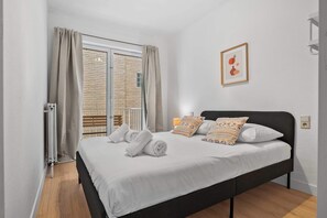 A hotel room with a bed, a window with curtains, a radiator, and a wall-mounted light switch. - Casiola - Stylish 2BR Apartment in Knokke (Knokke-Heist)