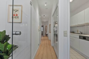 A hallway with a framed sign, a plant, a door, and a kitchen area with cabinets and a dishwasher. - Casiola - Stylish 2BR Apartment in Knokke (Knokke-Heist)