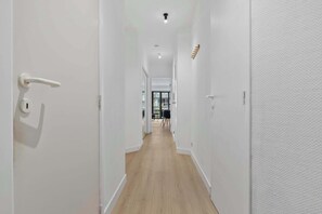 A narrow hallway with white walls and wooden flooring, leading to a dining area with a table and chairs. - Casiola - Stylish 2BR Apartment in Knokke (Knokke-Heist)