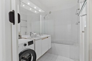 Een moderne badkamer met een wasmachine, twee wasbakken, een badkuip en een grote spiegel.