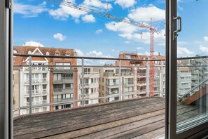Blick vom Balkon mit Holzboden auf ein Wohngebiet mit verschiedenen Gebäuden, darunter ein Kran in der Ferne.