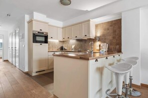 A modern kitchen with a central island, white cabinetry, and a tiled backsplash. - Casiola - Charming Duplex with Terrace in Knokke (Knokke-Heist)