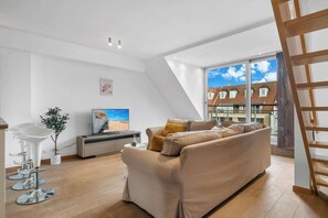 A modern living room with a sofa, a TV, a plant, and a staircase. - Casiola - Charming Duplex with Terrace in Knokke (Knokke-Heist)