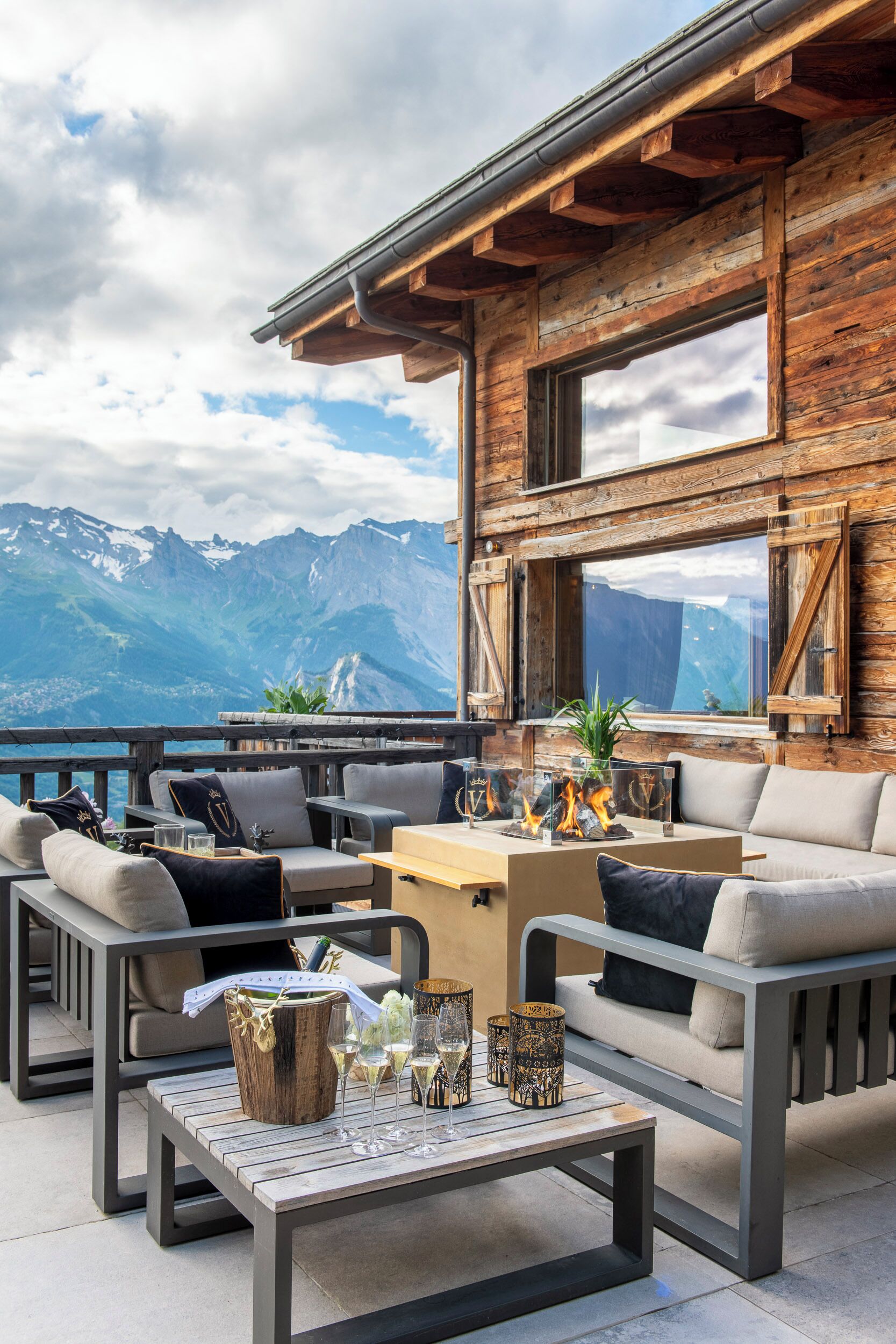 Une terrasse en bois avec des sièges d’extérieur, une table avec des verres et une bouteille, et une vue sur la montagne.
