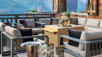 Une terrasse en bois avec des sièges d’extérieur, une table avec des verres et une bouteille, et une vue sur la montagne.
